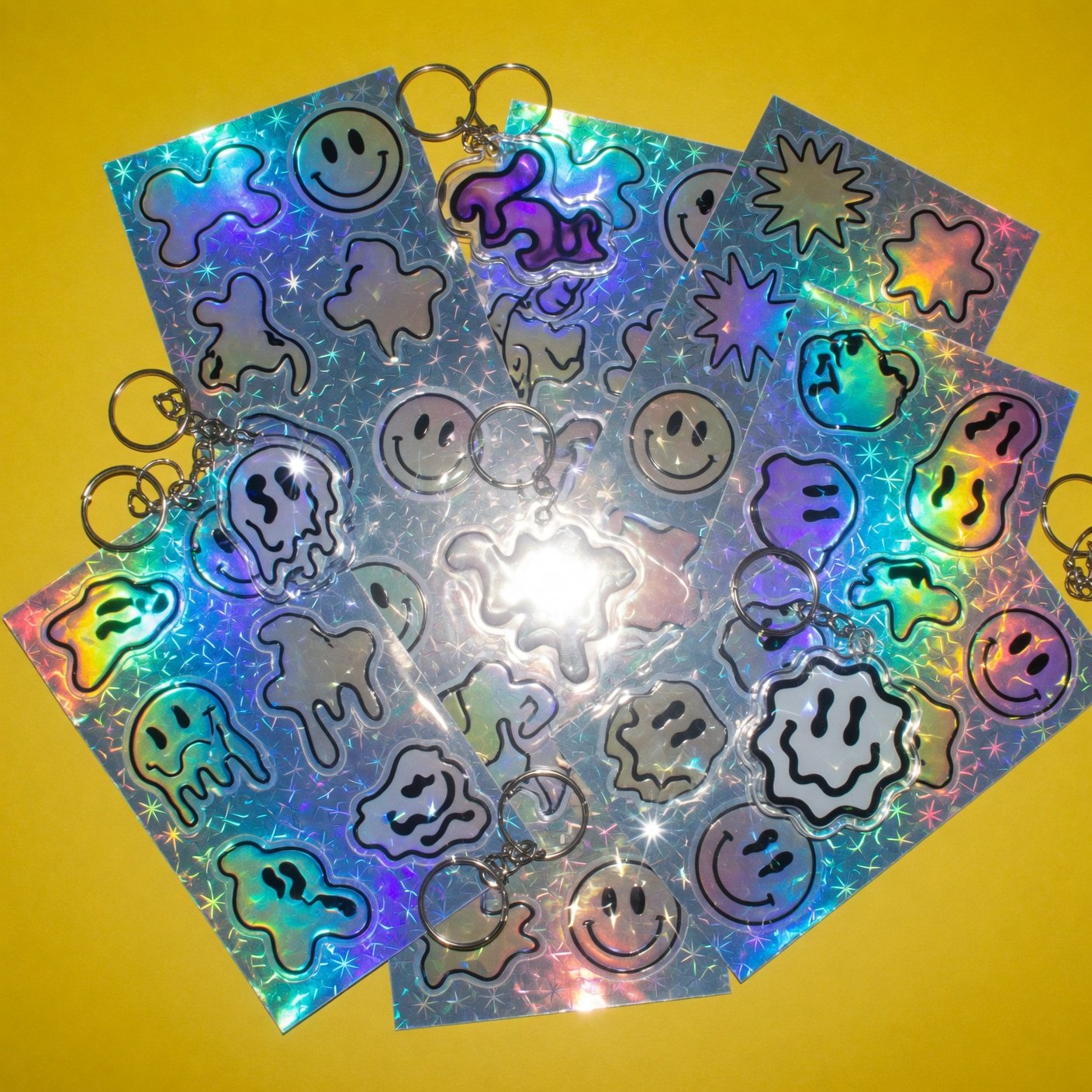 Planchas de stickers holográficos con caritas derretidas sobre fondo amarillo