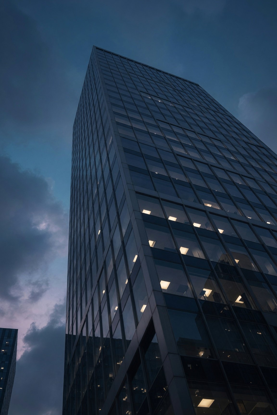 Torre de oficinas vista desde abajo al atardecer, con algunas ventanas iluminadas